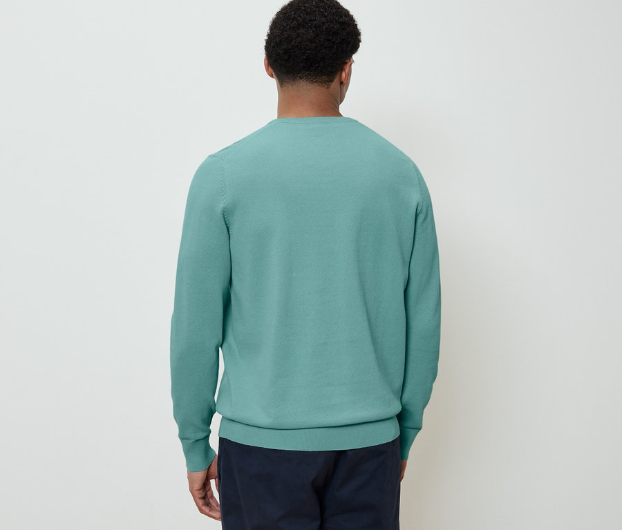 Mężczyzna tyłem do kamery ma na sobie sweter i granatowe spodnie.