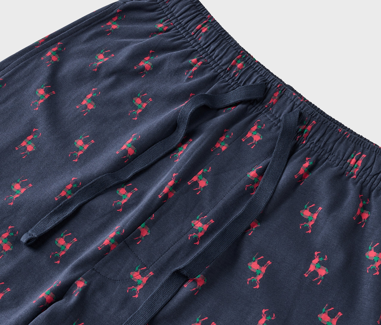 Szczegół niebieskich spodni od piżamy z czerwonymi reniferami i zielonymi siodłami.