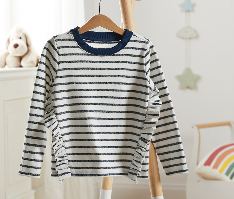 Bluza dresowa w paski z brokatowymi elementami wisi na drewnianym wieszaku.