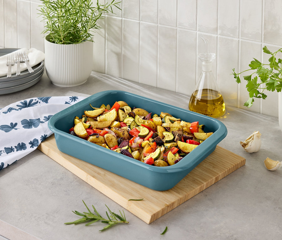 Pieczone ziemniaki z warzywami w niebieskim naczyniu do pieczenia na drewnianej desce.