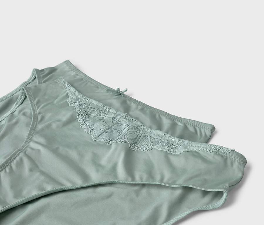 Dwie jasnozielone majtki z koronką leżą na sobie.