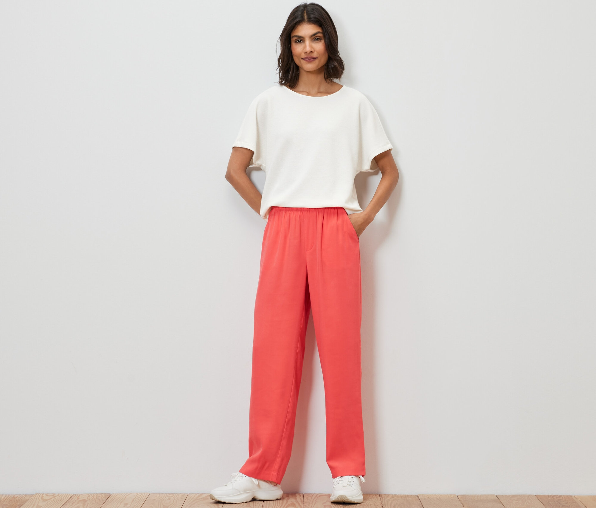 Kobieta stoi z rękami w kieszeniach spodni z tkaniny.