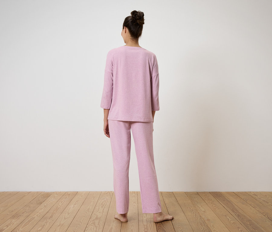 Kobieta stoi tyłem do kamery, ubrana w różową piżamę.