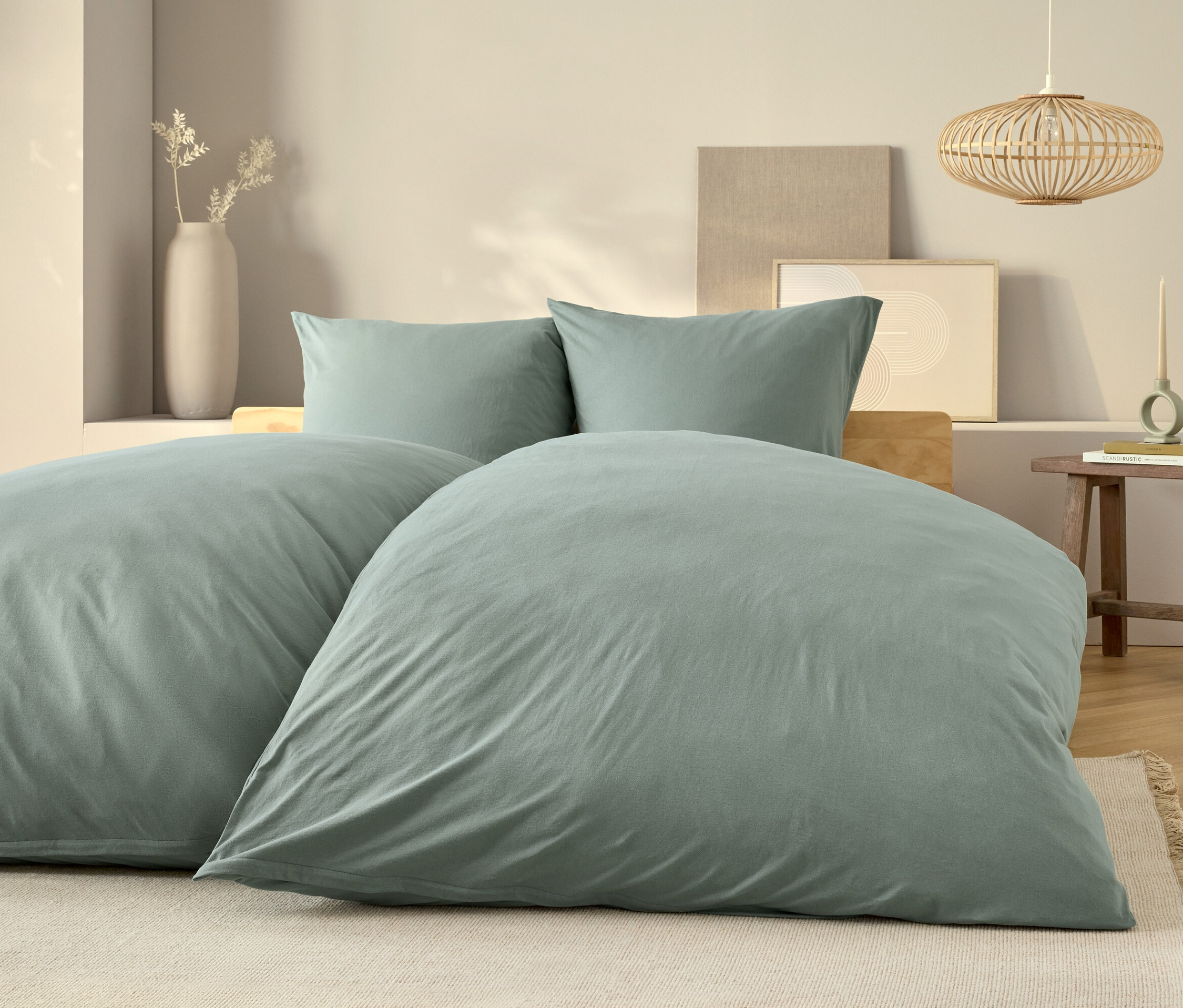 Jasnoniebieska pościel leży na łóżku z dwiema poduszkami i drewnianym stolikiem nocnym.