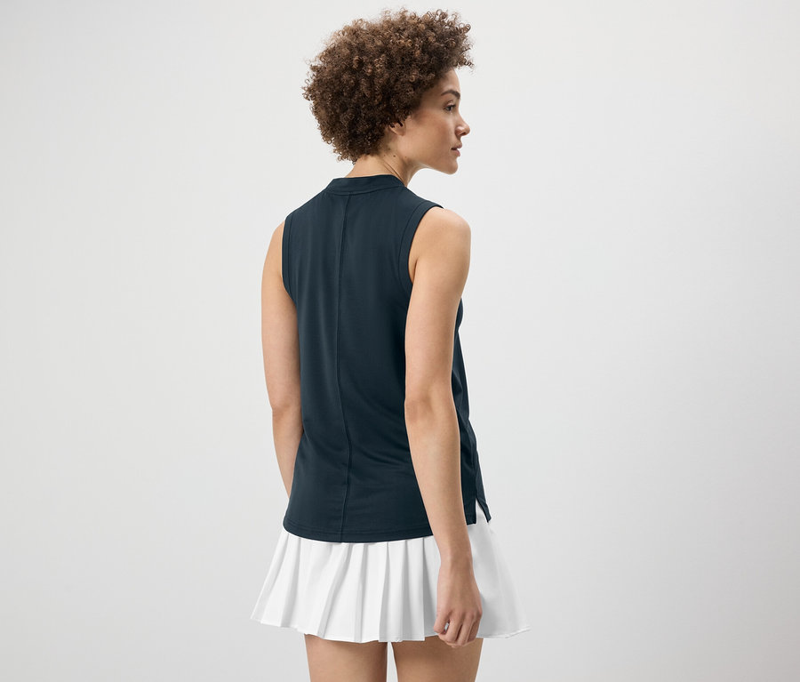 Kobieta tyłem do kamery ma na sobie granatowy top funkcyjny i białą spódnicę.