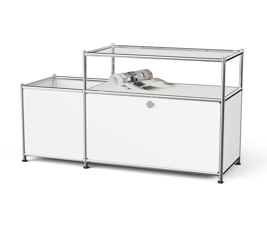 Biały modułowy system przechowywania z chromowaną ramą i szklanymi półkami, na górnej półce leży zwinięty magazyn.