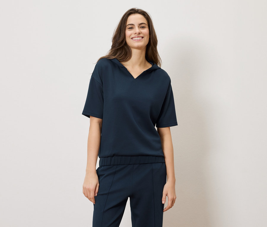 Uśmiechnięta brunetka w granatowym komplecie: bluzce z krótkim rękawem i spodniach.