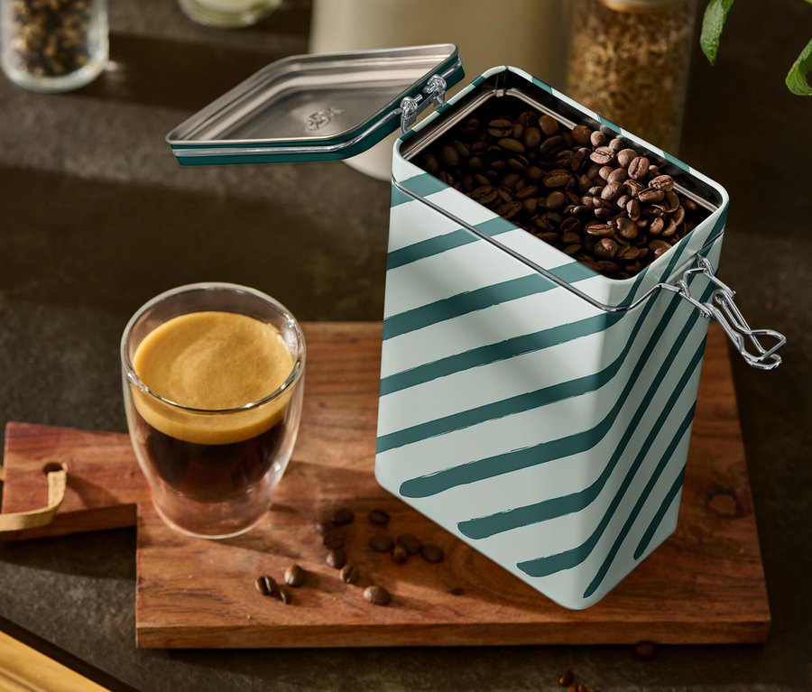 Szklanka espresso i otwarty, paskowany pojemnik na kawę stoją na drewnianej desce.