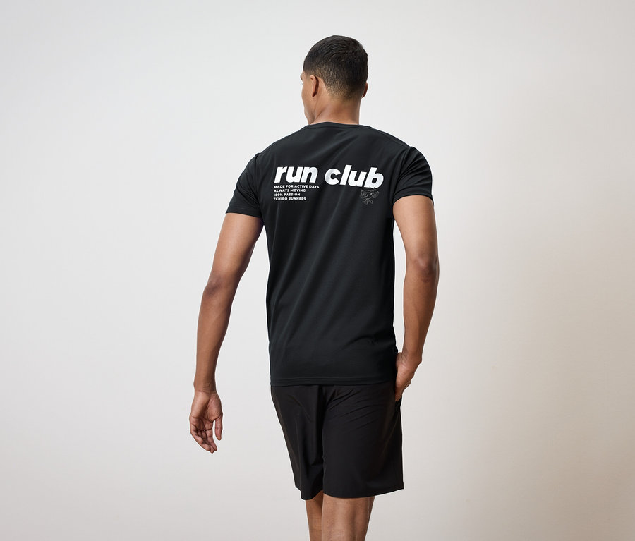 Mężczyzna od tyłu, ubrany w czarną koszulkę z napisem "run club" i czarne szorty.