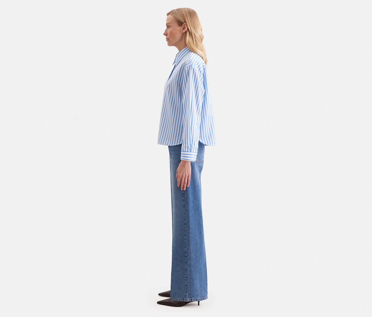 Kobieta z profilu nosi niebiesko-białą bluzkę koszulową oversize Seidensticker i szerokie jeansy.
