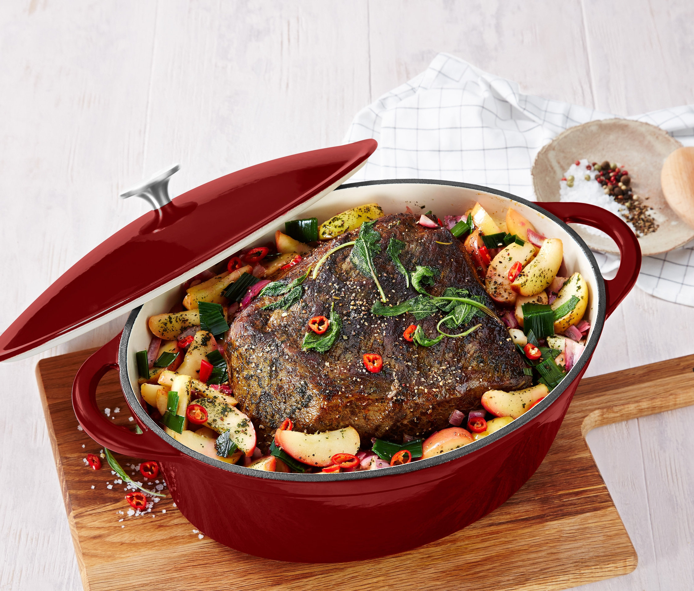 Pieczeń z owocami i warzywami w garnku z żeliwa. Czerwona pokrywa jest częściowo odkryta.