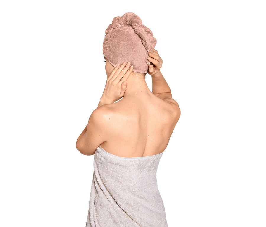 Kobieta poprawia różowy ręcznik turban na głowie, owinięta ręcznikiem.