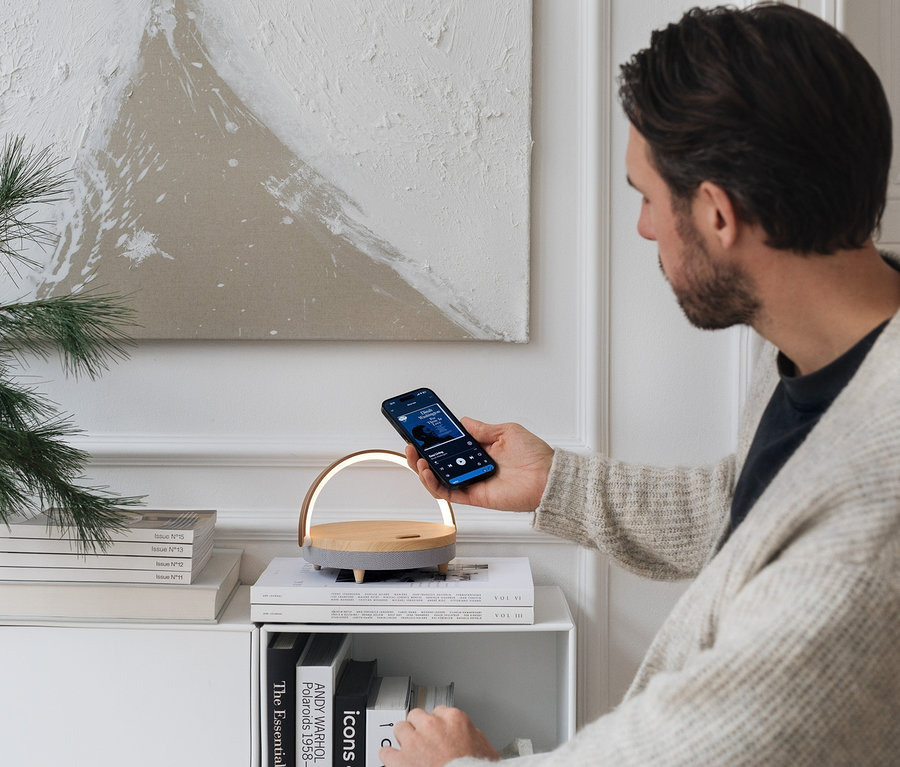 Mężczyzna trzyma telefon nad głośnikiem Bluetooth z bezprzewodową ładowarką i lampką LED.
