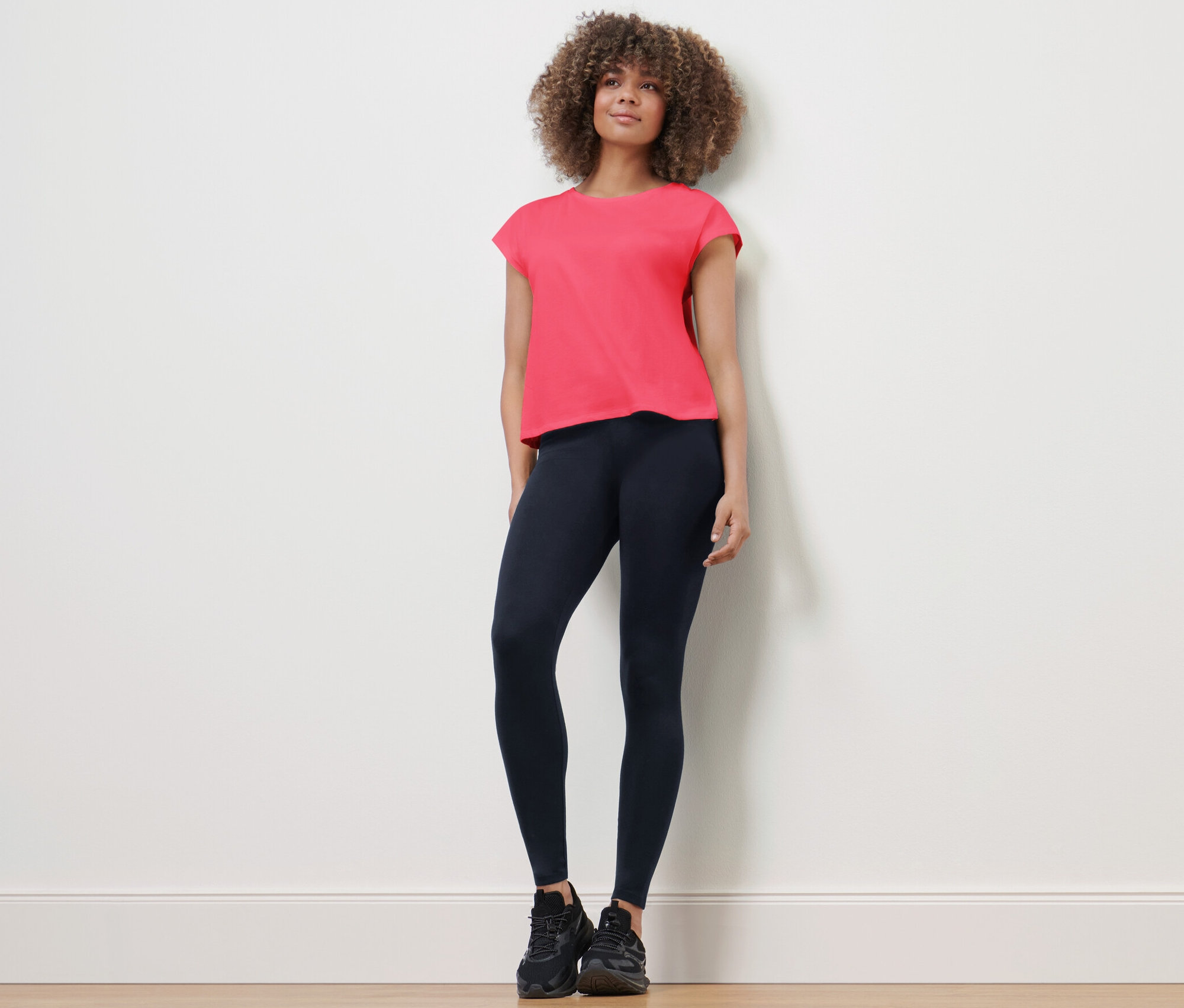 Kobieta stoi, ubrana w legginsy sportowe i koszulkę.
