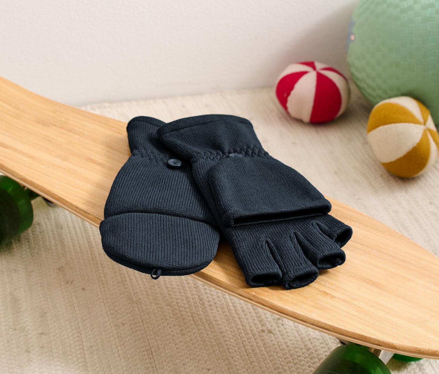 Rękawiczki polarowe z klapką leżą na deskorolce obok piłek.