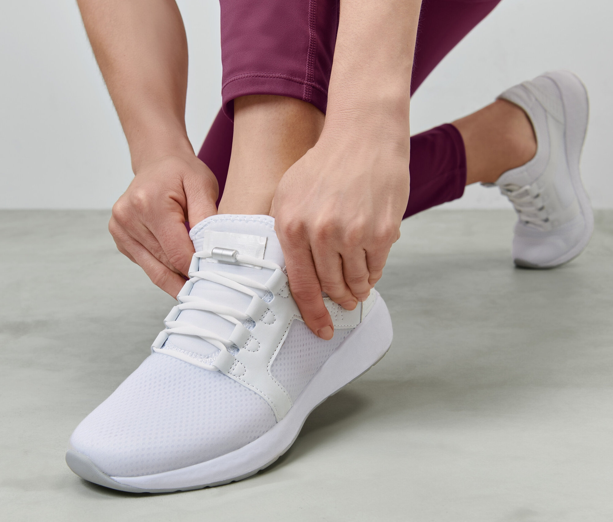 Kobieta zawiązuje elastyczne sznurowadła na białym bucie.