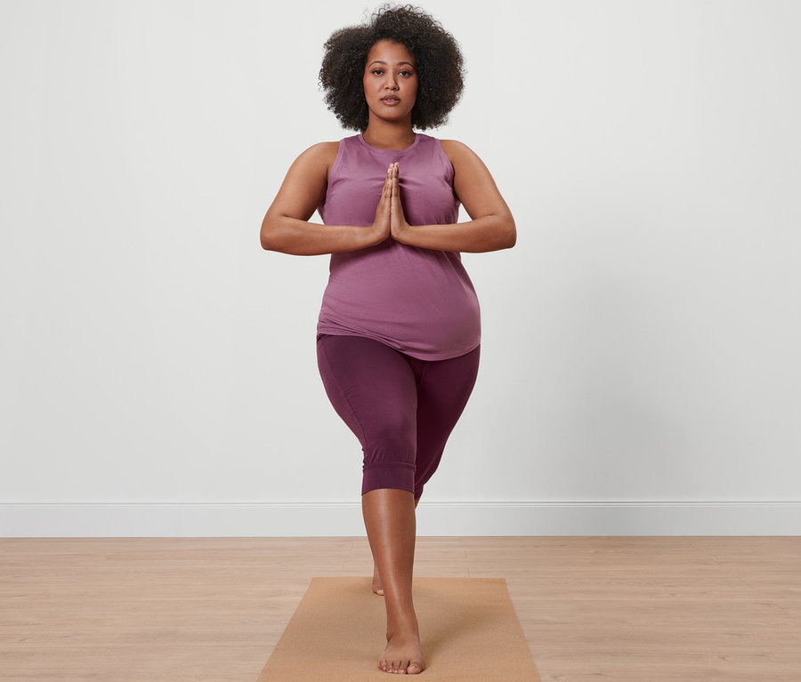 Kobieta w liliowych spodniach do jogi o długości 3/4 i liliowym topie sportowym stoi na macie do jogi.