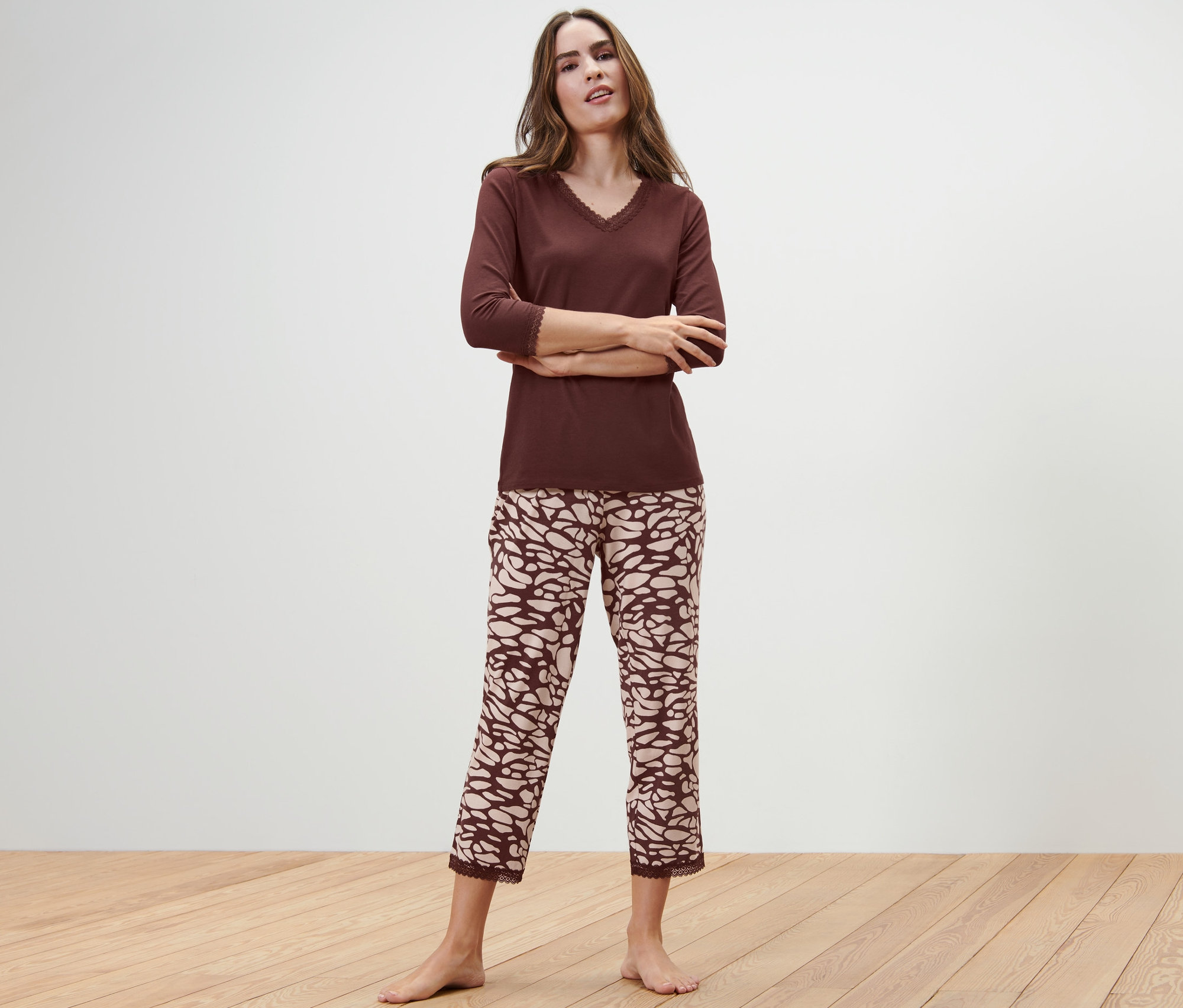 Kobieta w piżamie stoi ze skrzyżowanymi ramionami na tle białej ściany.