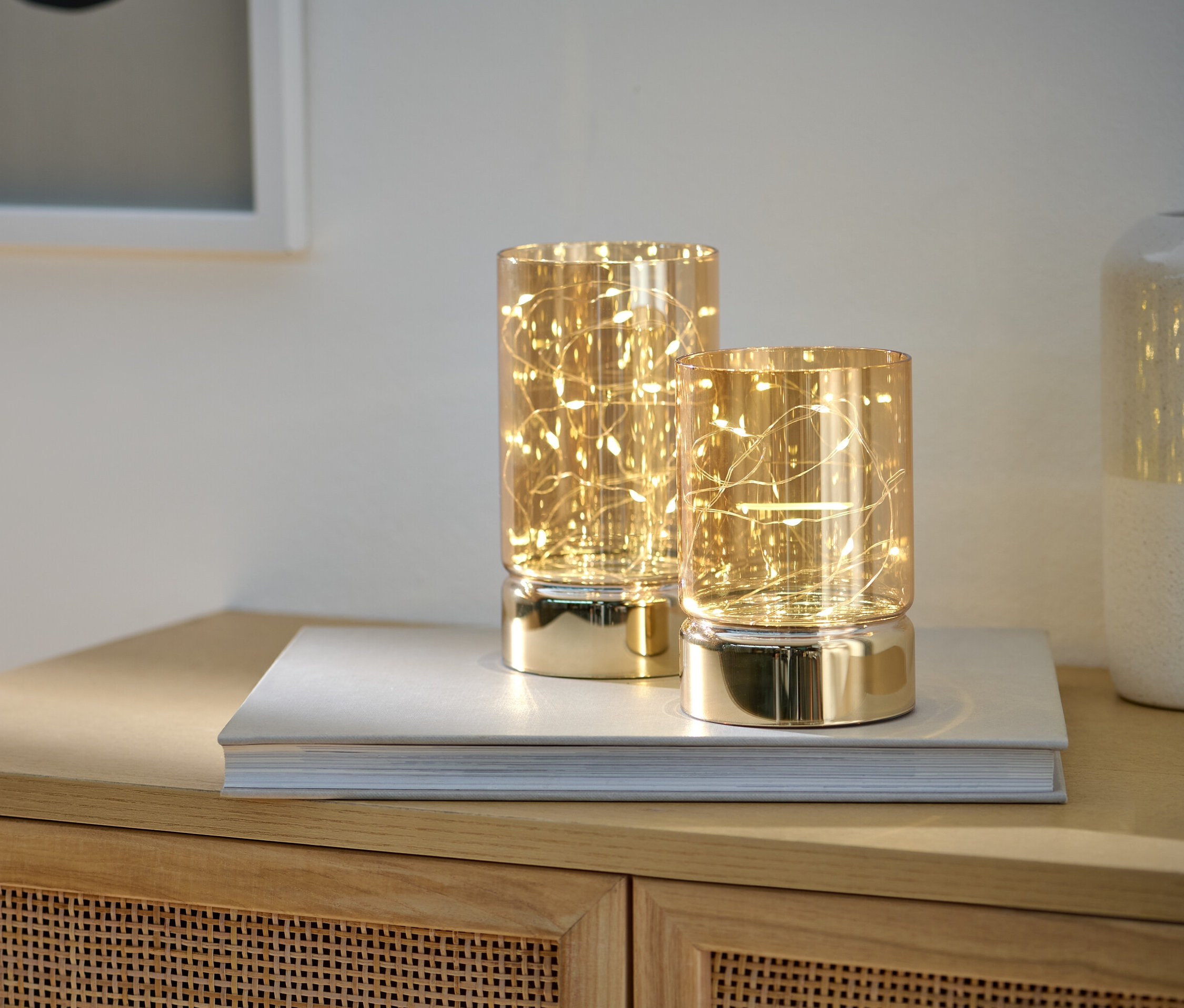 Dwa szklane lampiony LED stoją na książce na szafce.
