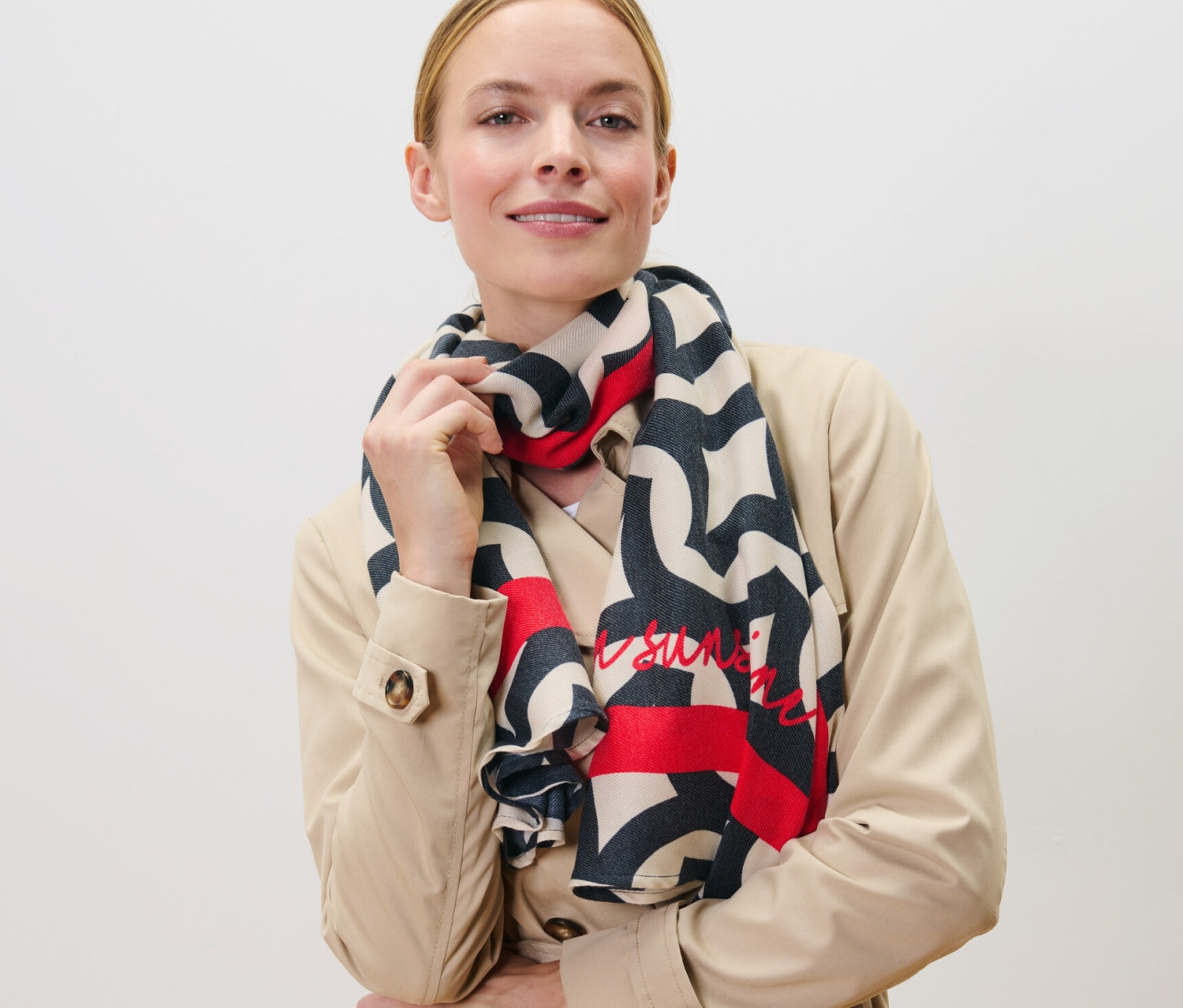 Kobieta pozuje w bezowym trenczu z wzorzystym szalem z tkaniny.