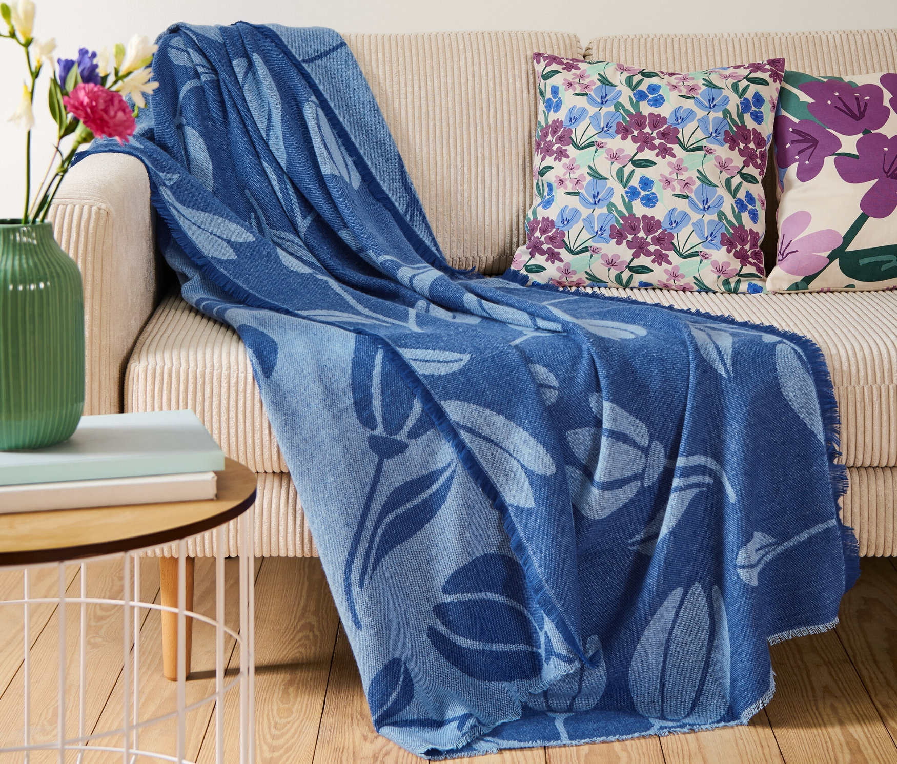 Na beżowej sofie leży niebieski koc z frędzlami.