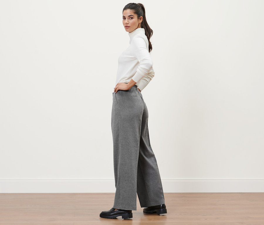 Kobieta pozuje w szarych spodniach z tkaniny i białym golfie.