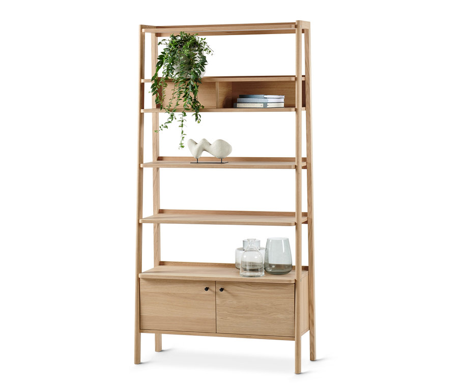 Jasny, drewniany regał z pięcioma otwartymi półkami i szafką z dwojgiem drzwi. Na półkach stoją rośliny, książki, wazony i rzeźba.