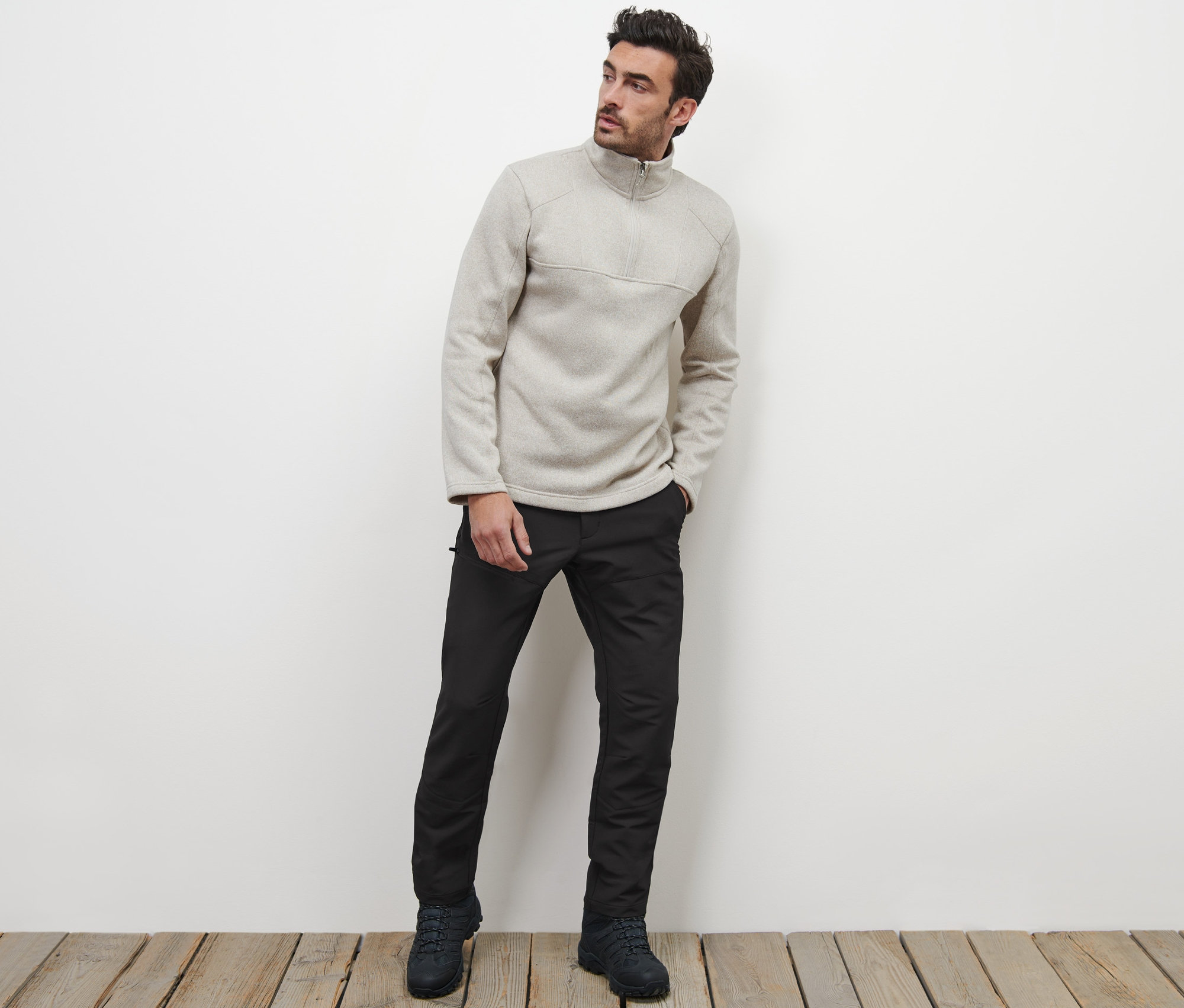 Mężczyzna pozuje na drewnianej podłodze, ubrany w spodnie termoaktywne i bluzę z zamkiem błyskawicznym.