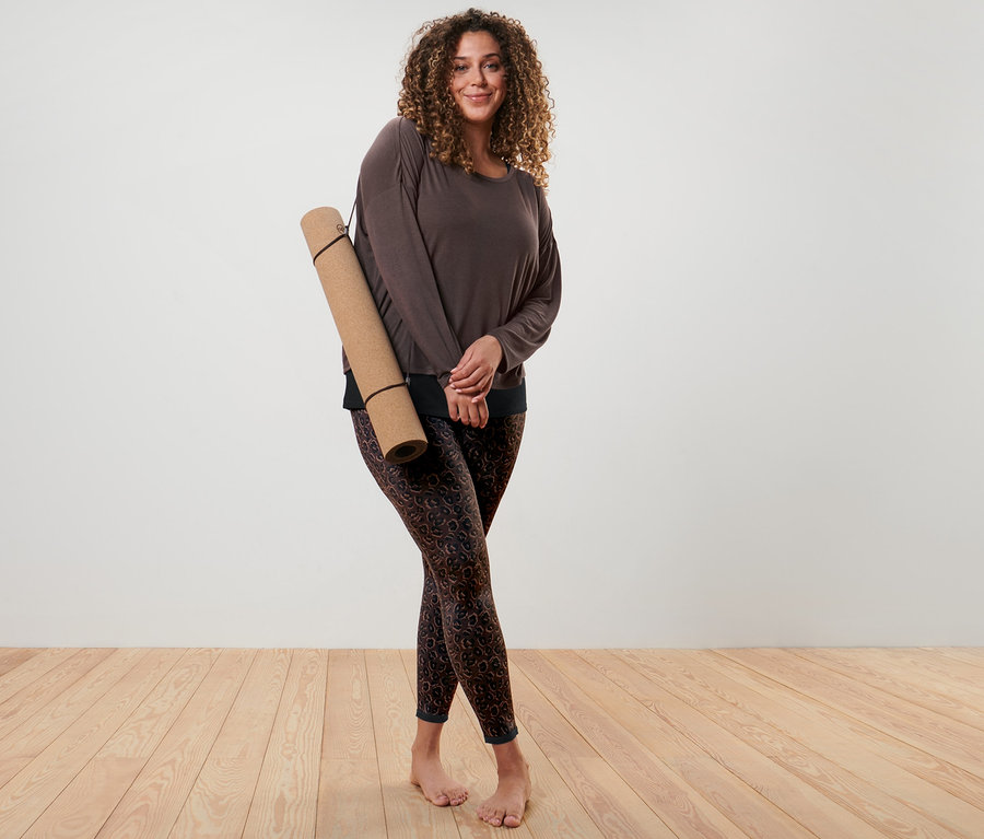 Kobieta pozuje w brązowej koszulce sportowej 2 w 1 i dwustronnych legginsach sportowych w kolorze czarnym i brązowym.