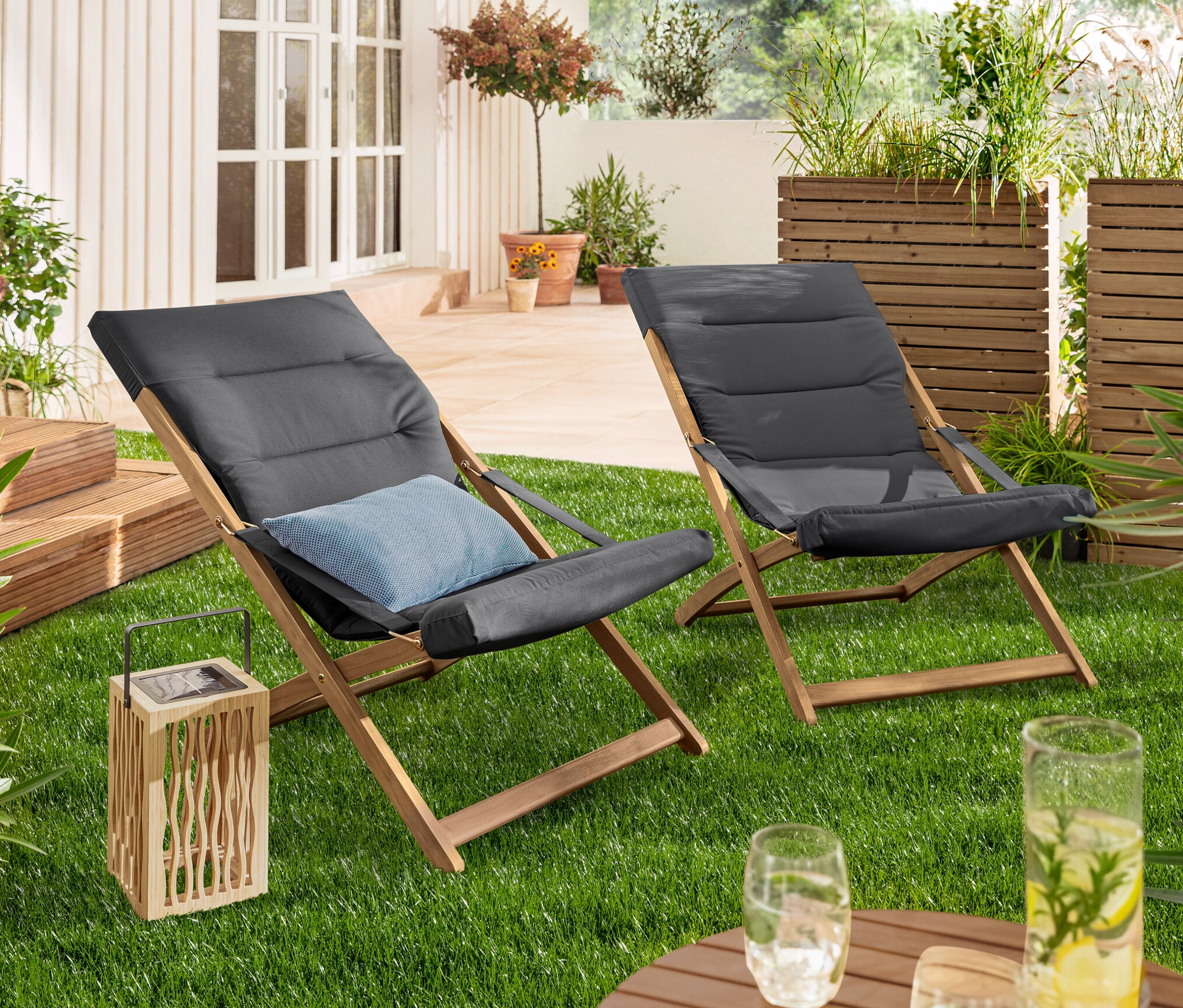 Na trawniku stoją lampion solarny i dwa antracytowe składane fotele wypoczynkowe.
