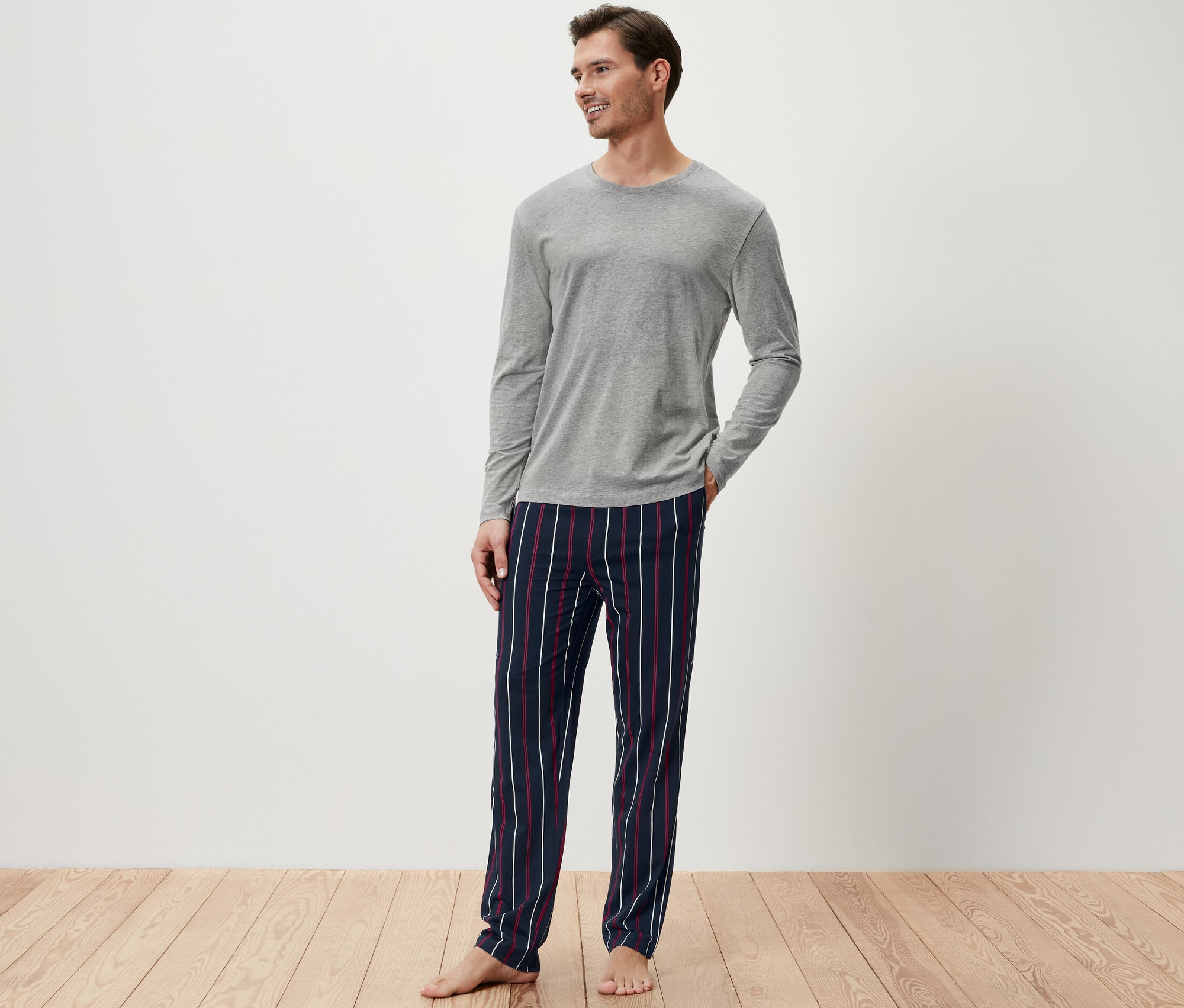 Mężczyzna w szarej piżamowej górze i spodniach w paski.