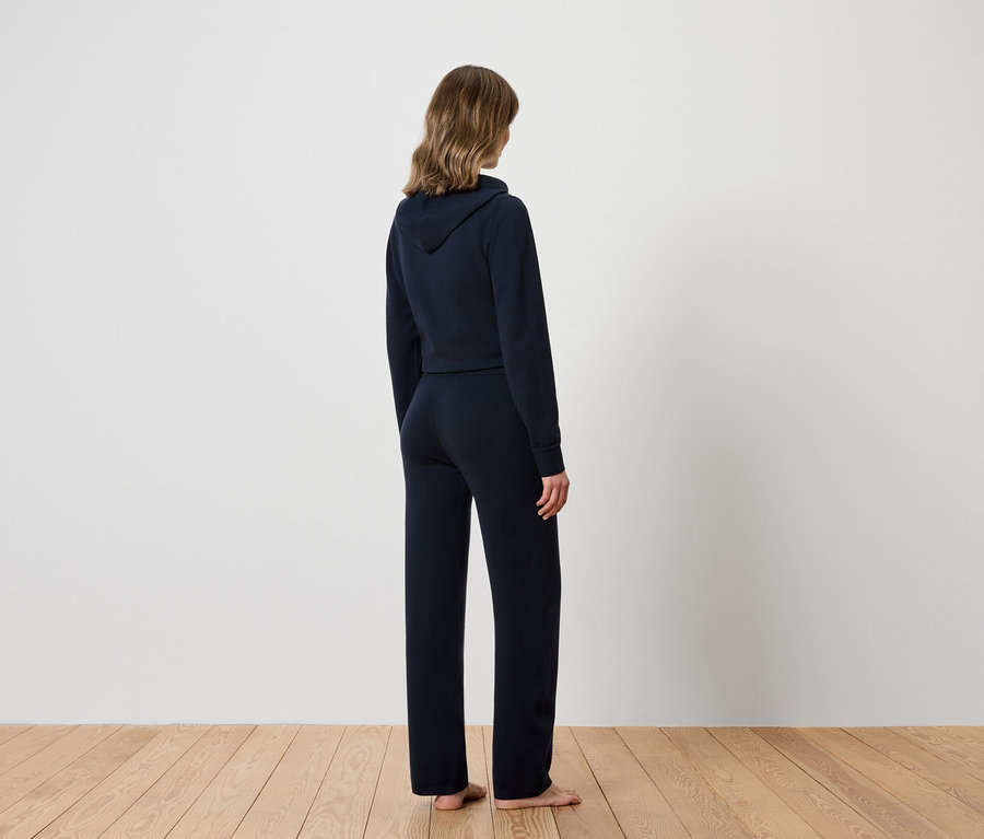 Kobieta tyłem do kamery ma na sobie granatową bluzę z kapturem i spodnie dresowe.