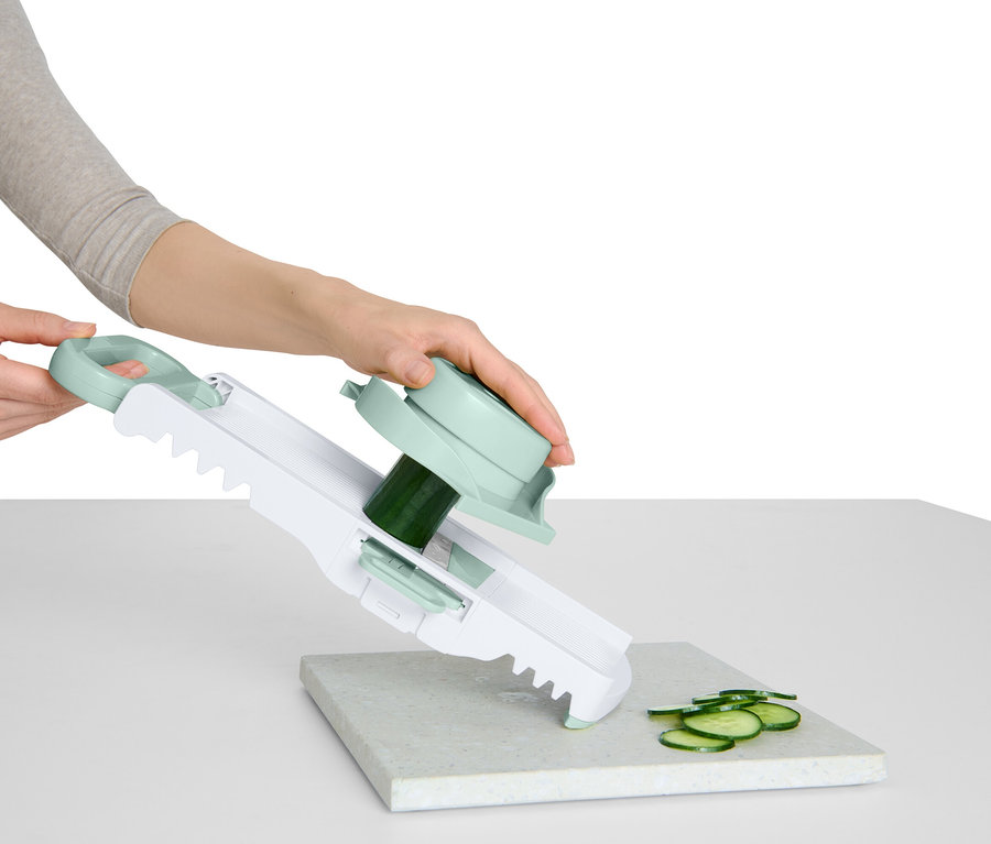 Kobieta kroi ogórek za pomocą krajalnicy do warzyw z uchwytem i obrotową przystawką.