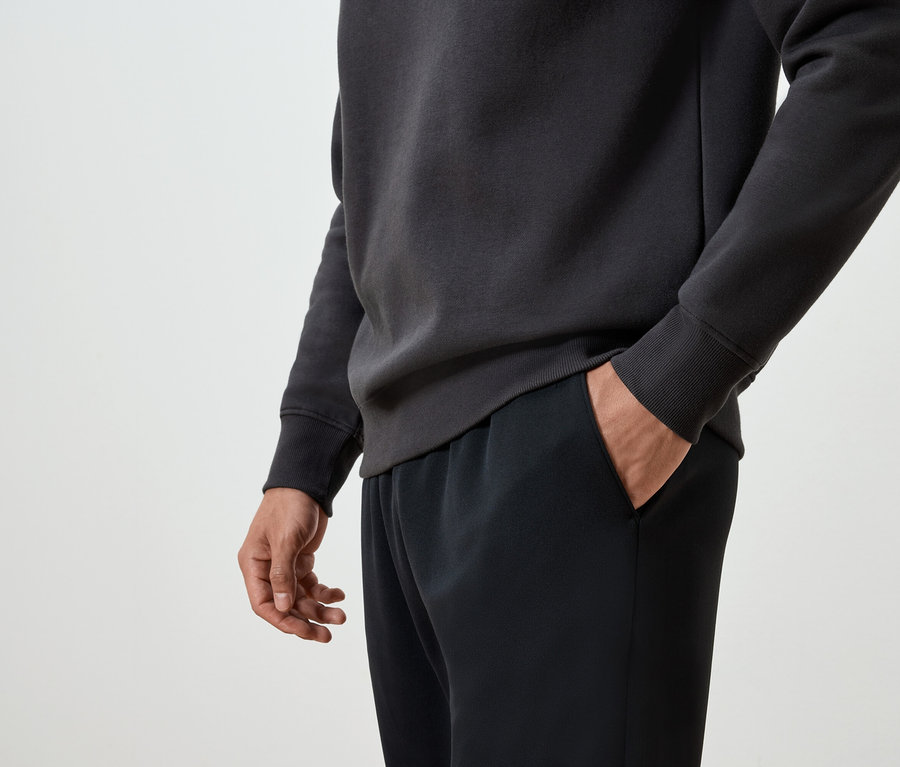 Mężczyzna trzyma rękę w kieszeni czarnych spodni dresowych i ma na sobie ciemnoszarą bluzę.