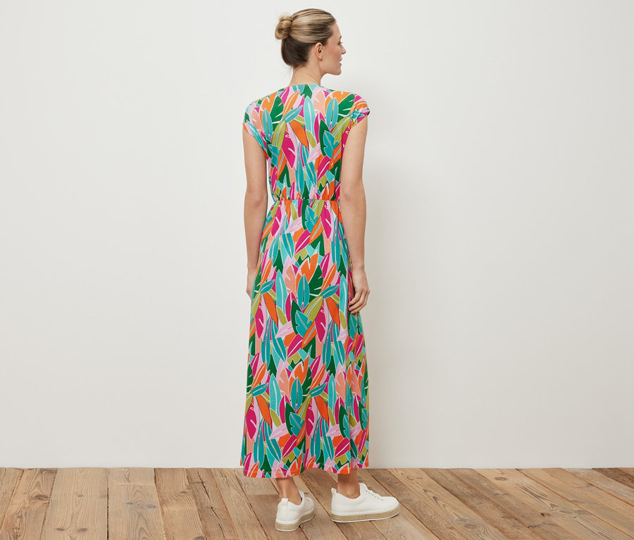 Kobieta stoi tyłem do aparatu, ubrana w sukienkę dżersejową z węzłem i białe tenisówki.