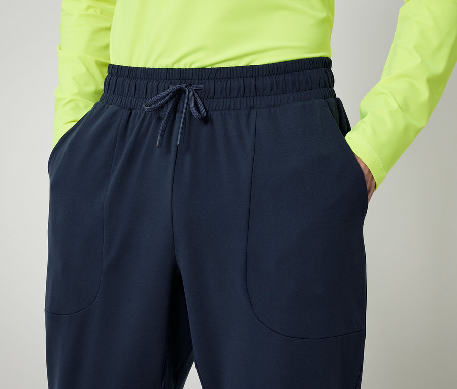 Osoba w neonowo zielonej koszuli i granatowych spodniach z rękami w kieszeniach.