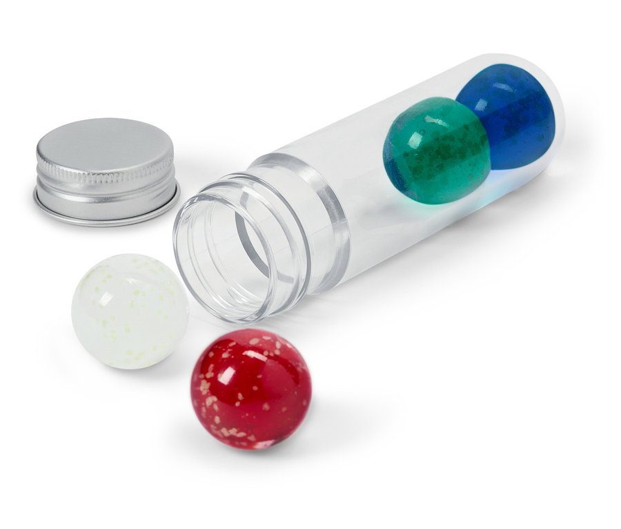 Przezroczysta tuba leży na boku z niebieską i zieloną kulką w środku, srebrna nakrętka obok oraz biała i czerwona kulka na zewnątrz.