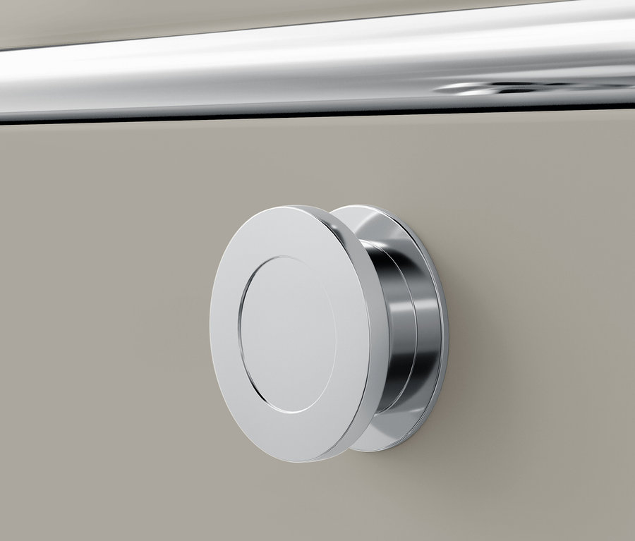 Detal chromowanego, okrągłego uchwytu na beżowej szufladzie.