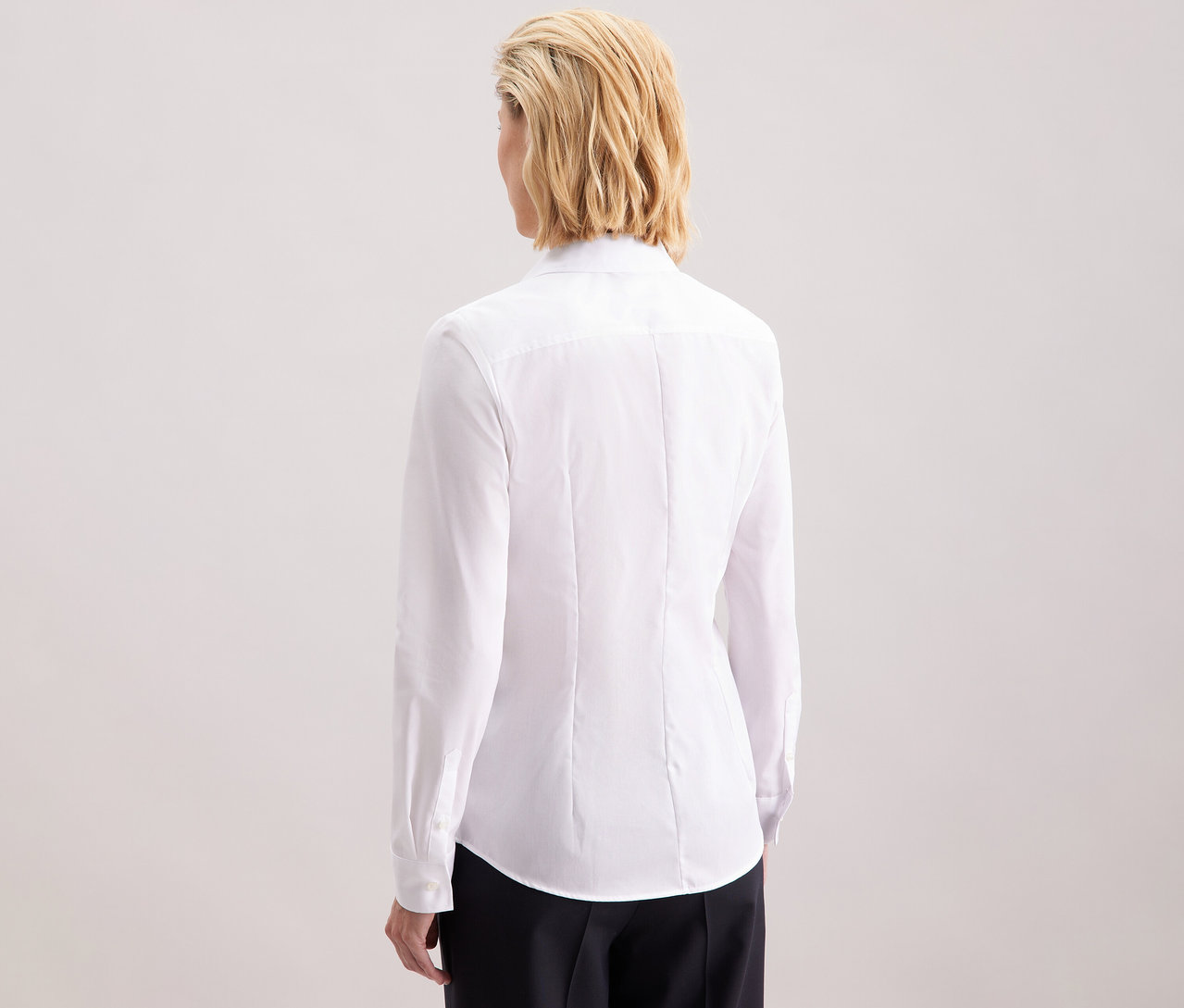 Widok z tyłu blondwłosej kobiety o długości do ramion, ubranej w białą, dopasowaną bluzkę Seidensticker Slim Fit non iron.