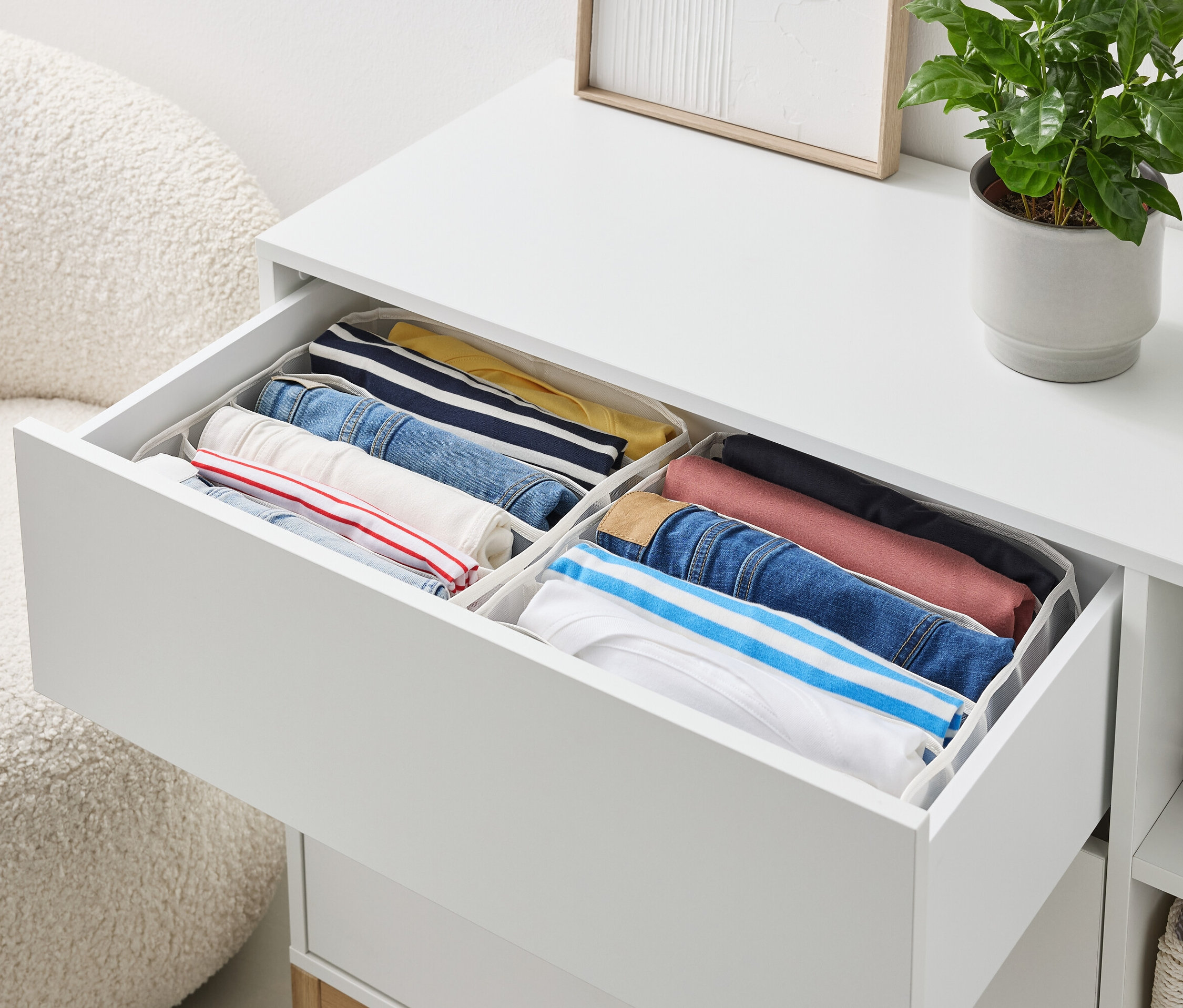 Otwarta szuflada białej komody zawiera starannie złożone ubrania w organizerach.