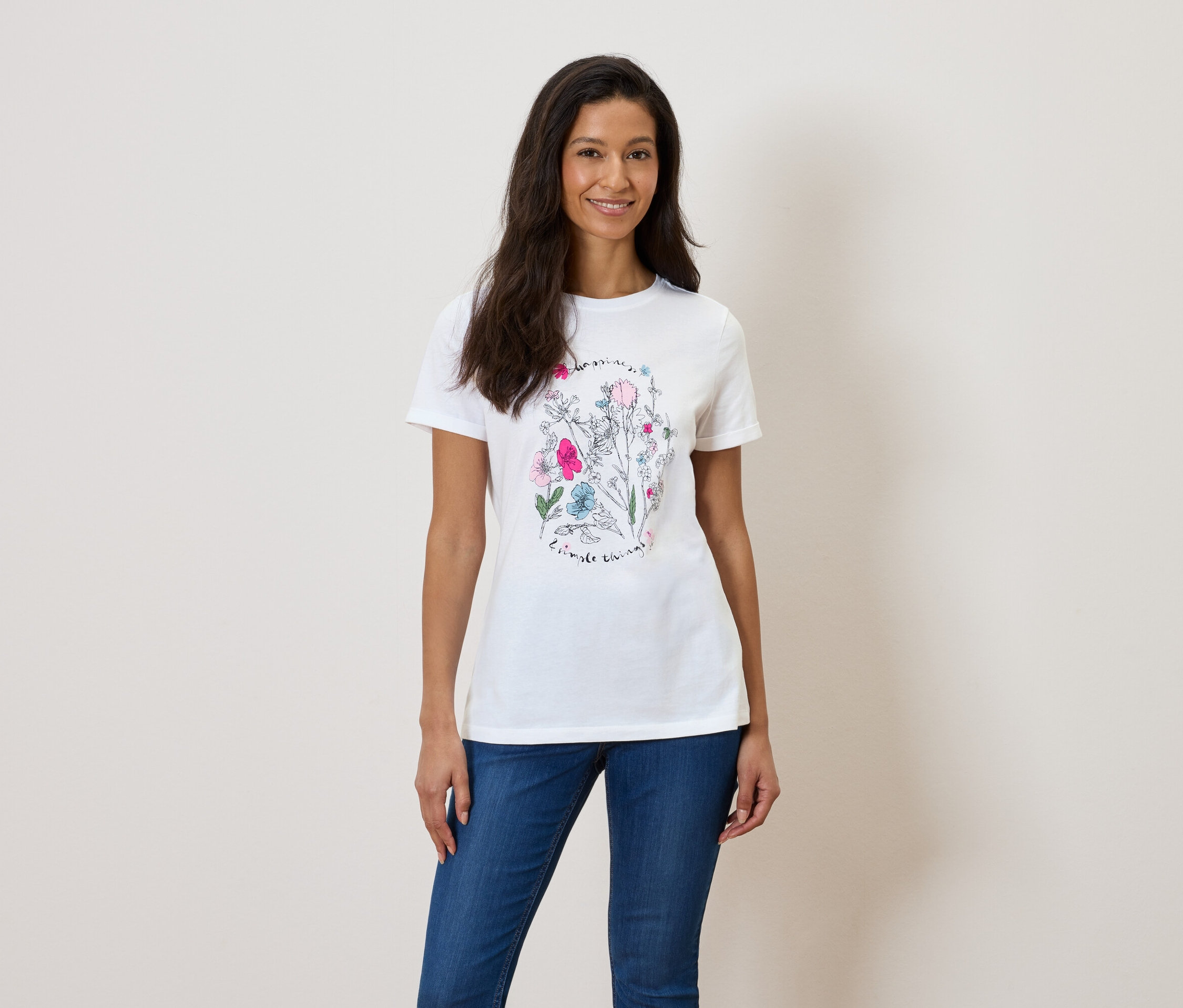 Kobieta ma na sobie białą koszulkę z kwiatowym nadrukiem i niebieskie dżinsy.