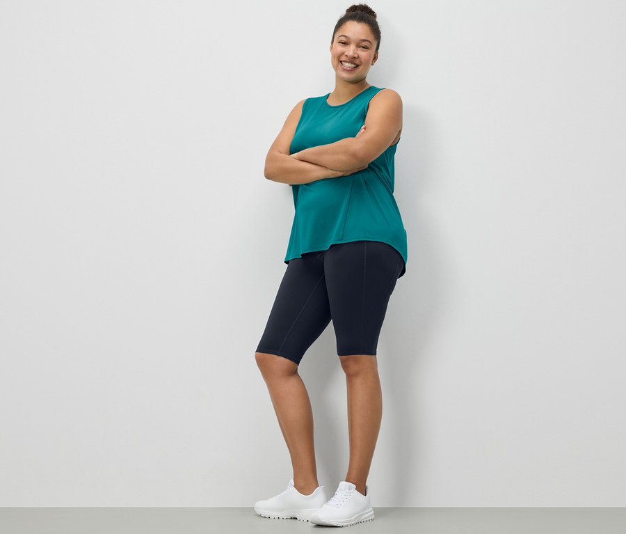 Kobieta pozuje w krótkich legginsach w kolorze granatowym i turkusowym topie sportowym z 2-częściowego zestawu.