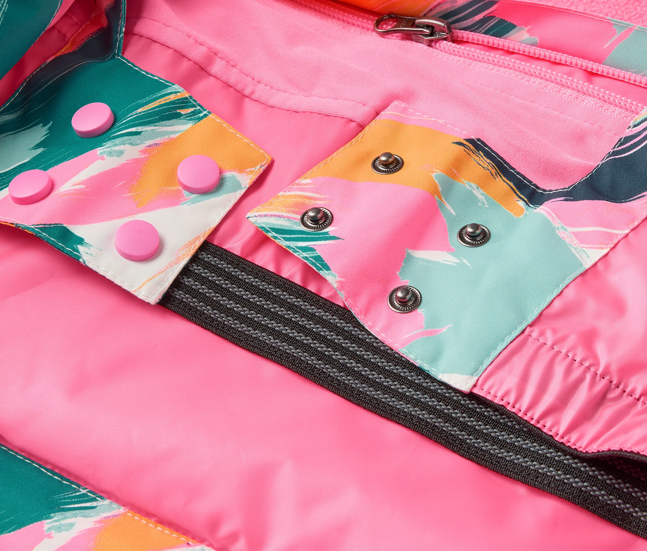 Szczegół kurtki z różową podszewką, kolorowymi wzorami i zatrzaskami.