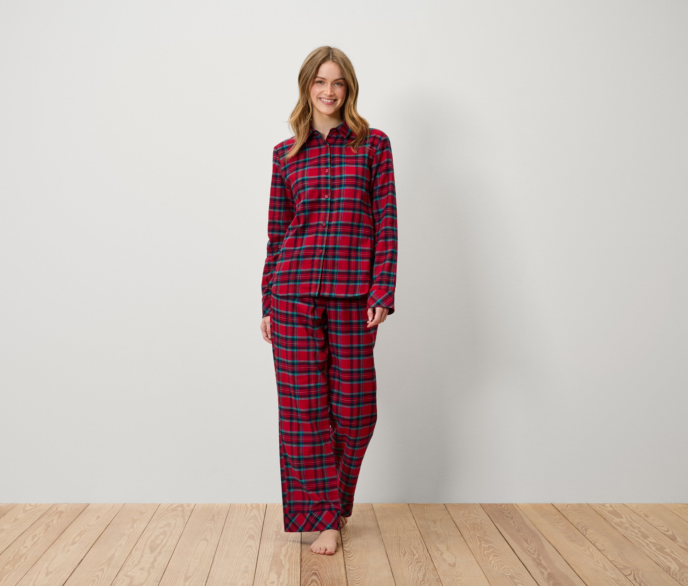 Kobieta stoi i uśmiecha się, ubrana w czerwoną piżamę w kratę.