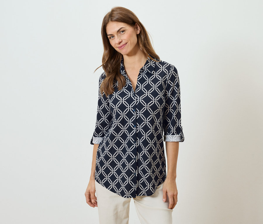 Kobieta ma na sobie granatową bluzkę z białym geometrycznym wzorem i beżowe spodnie.