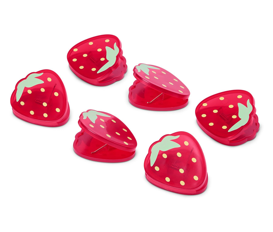 Sześć czerwonych spinaczy w kształcie truskawek leży na białej powierzchni.