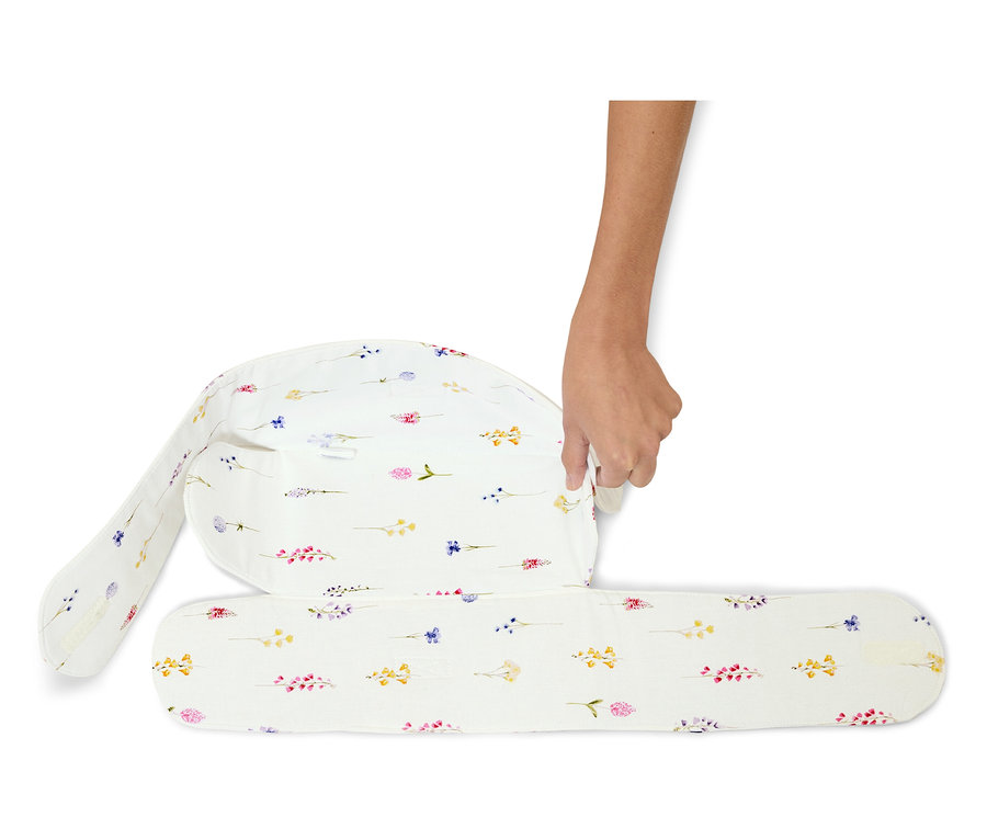 Ręka składa białą poduszkę do karmienia z kwiatowym wzorem.