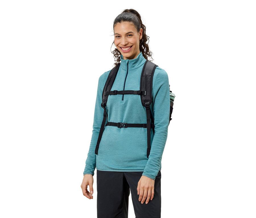 Uśmiechnięta kobieta w niebieskiej bluzce i czarnych spodniach z czarnym plecakiem.