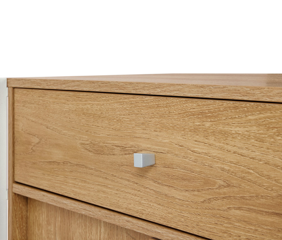 Zbliżenie na jasnobrązową drewnianą komodę ze srebrnym uchwytem.