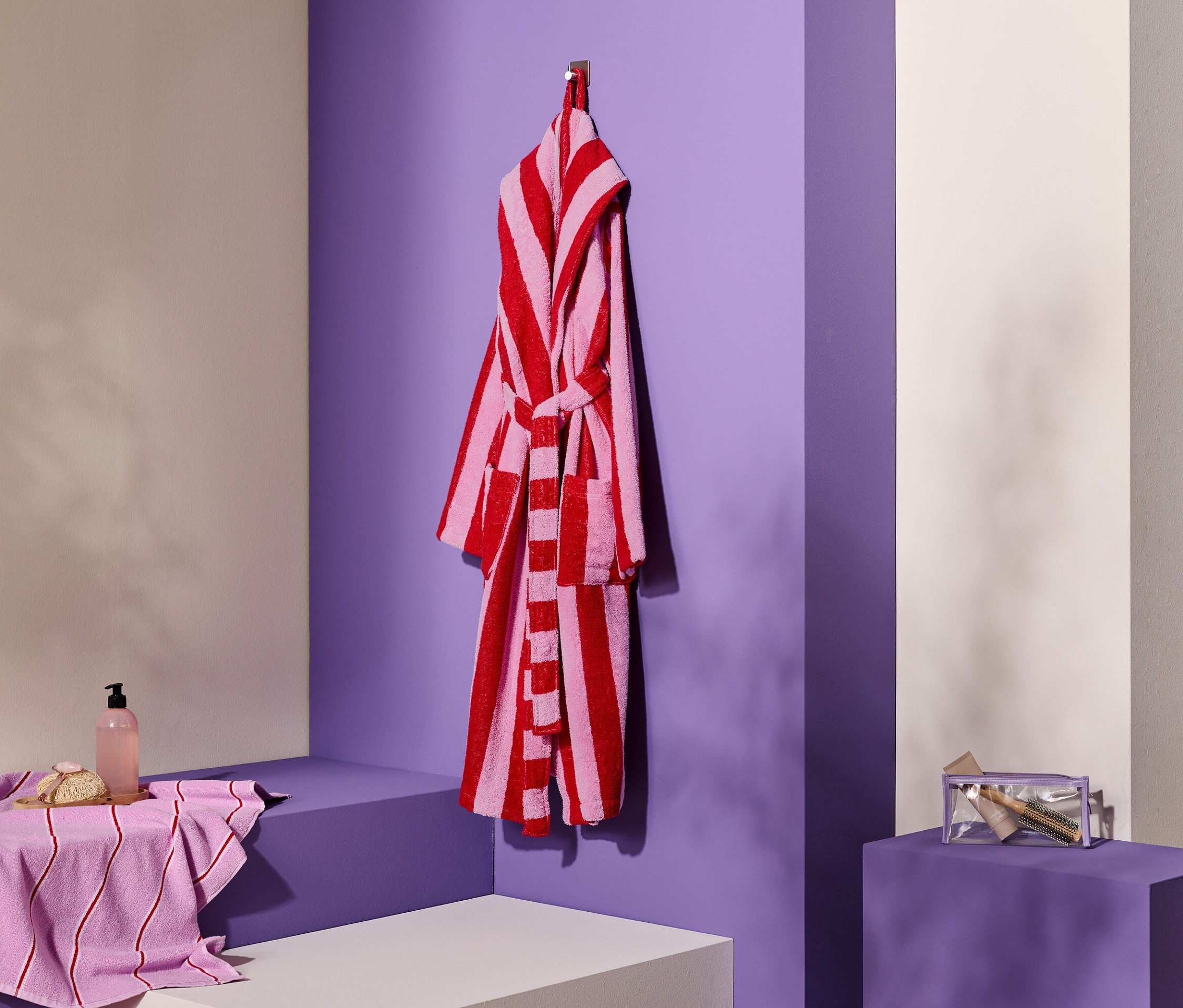 Pasiasty szlafrok wisi na haczyku obok ręcznika, mydła i kosmetyczki.